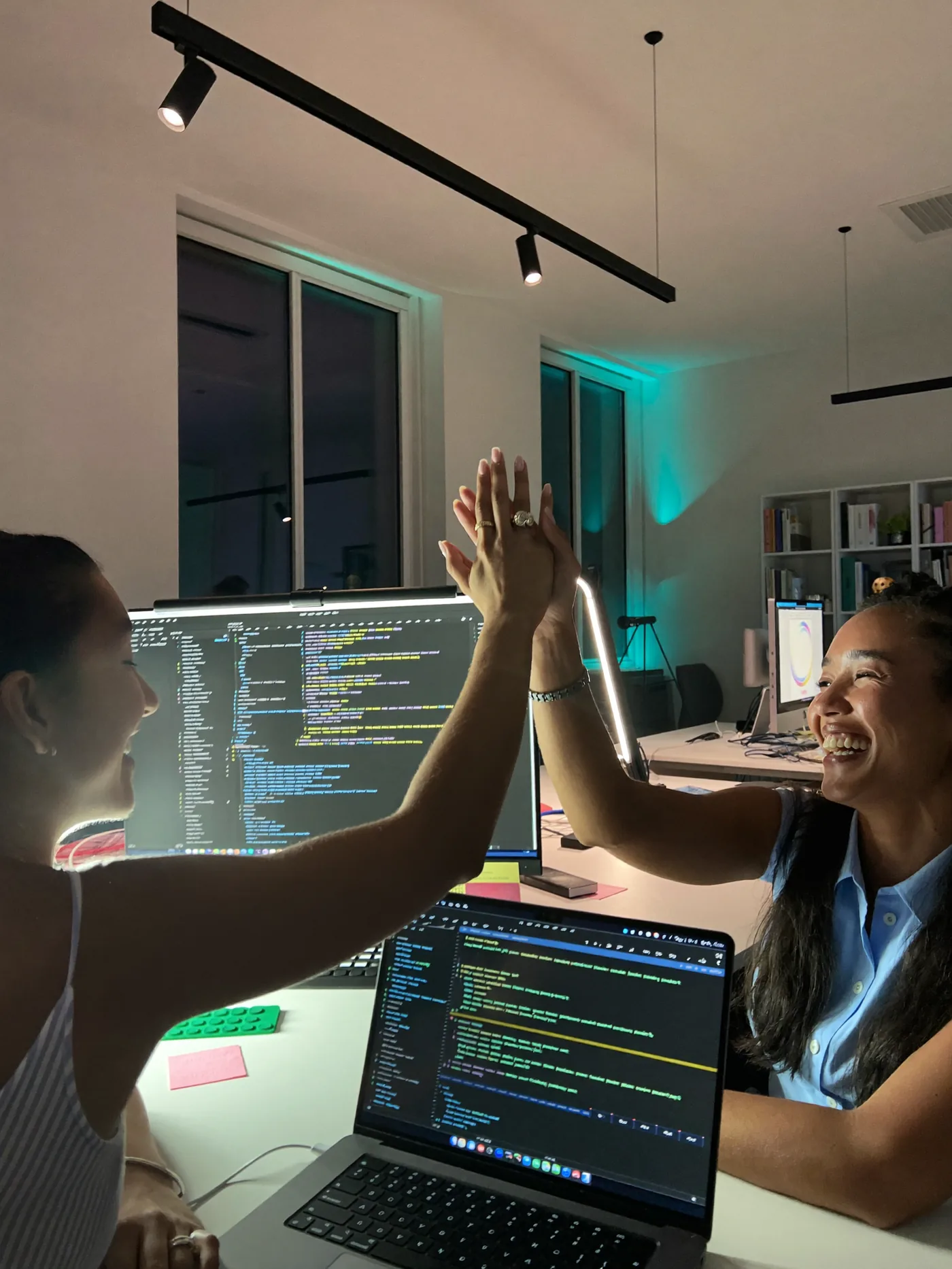 Duas pessoas comemorando com um high five diante de telas com código